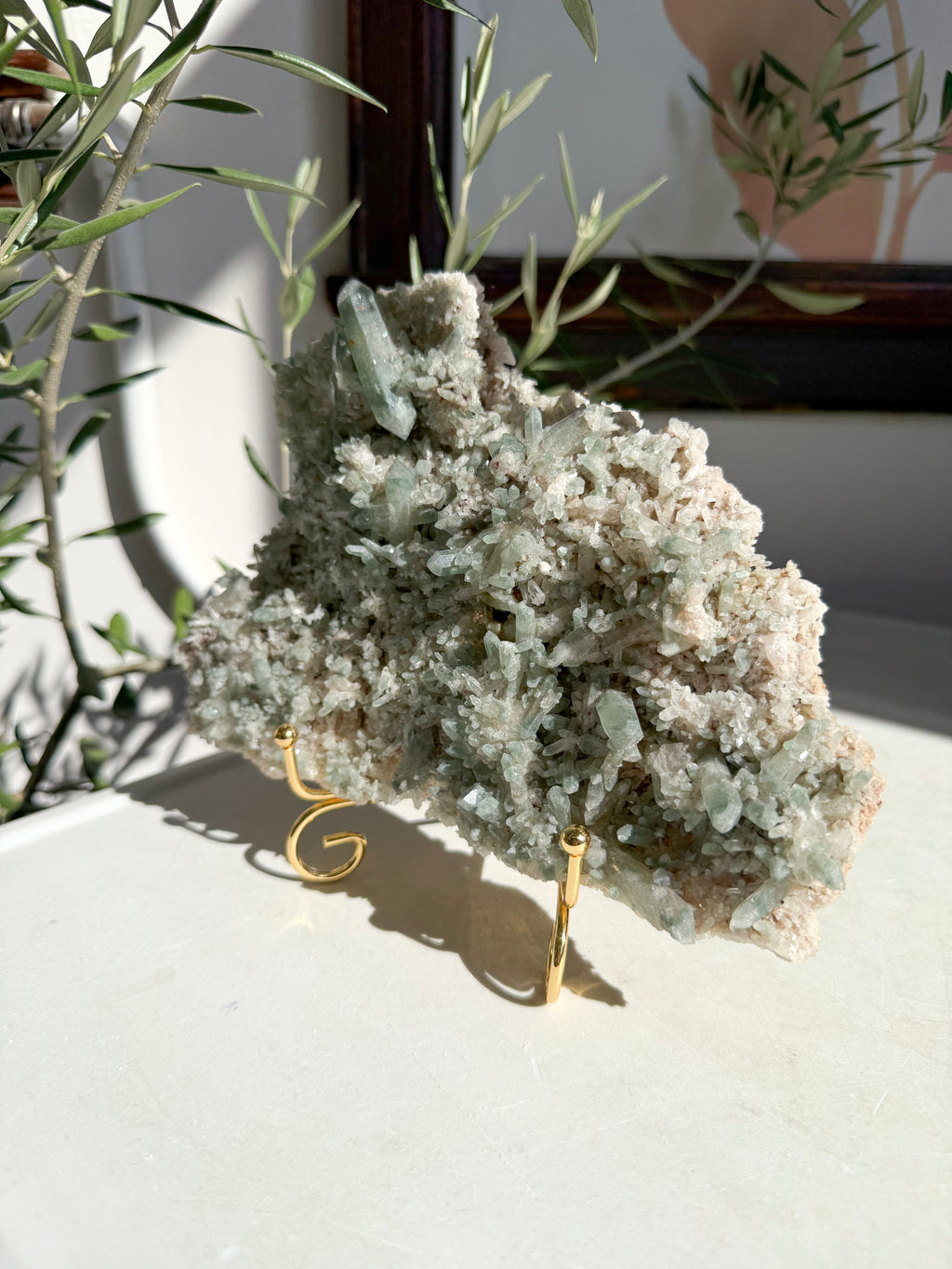 Chlorite and quartz cluster on gold stand sitting on marble counter