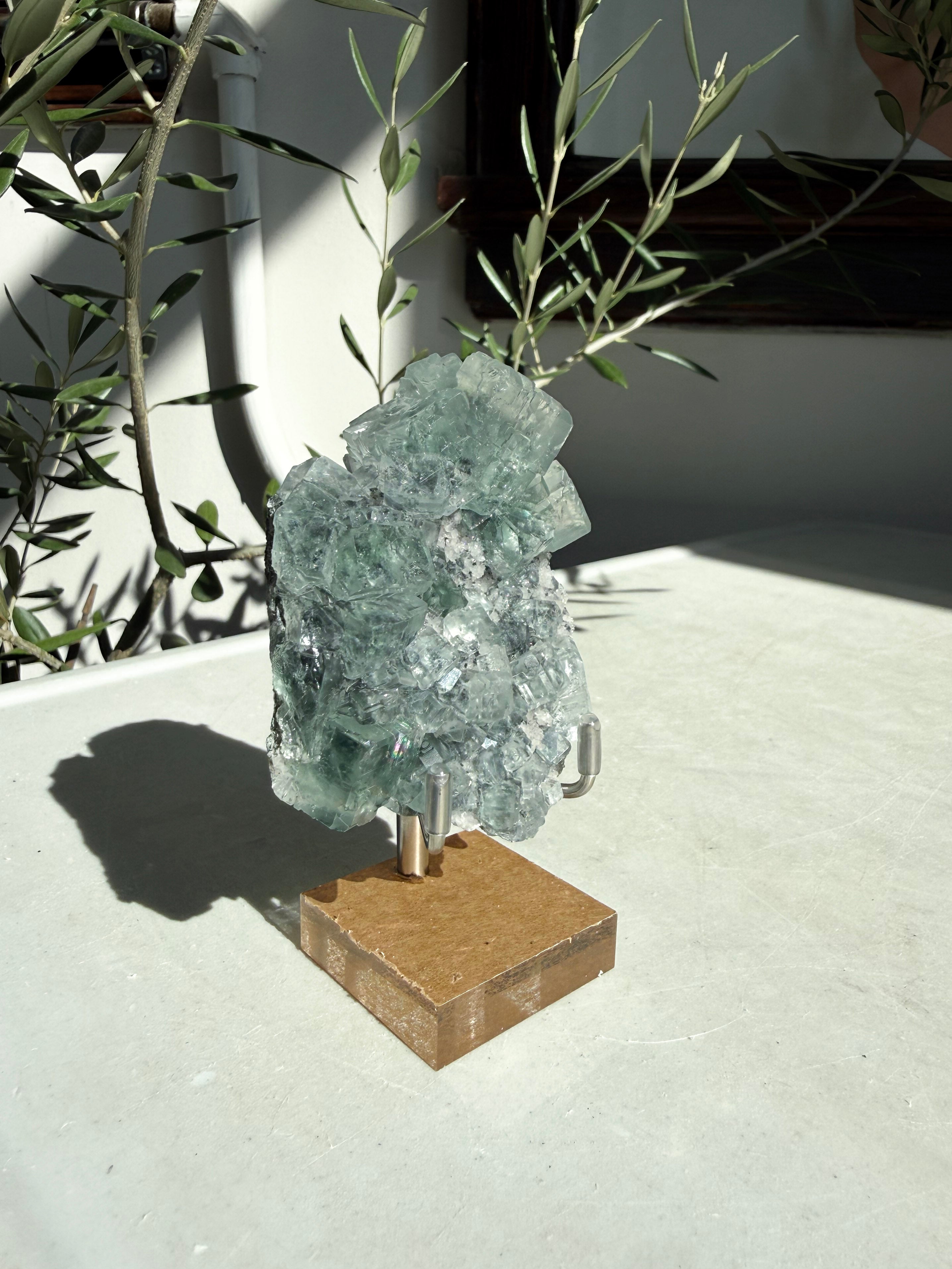 Glassy green cubic fluorite with druzy quartz on wood stand sitting on marble table