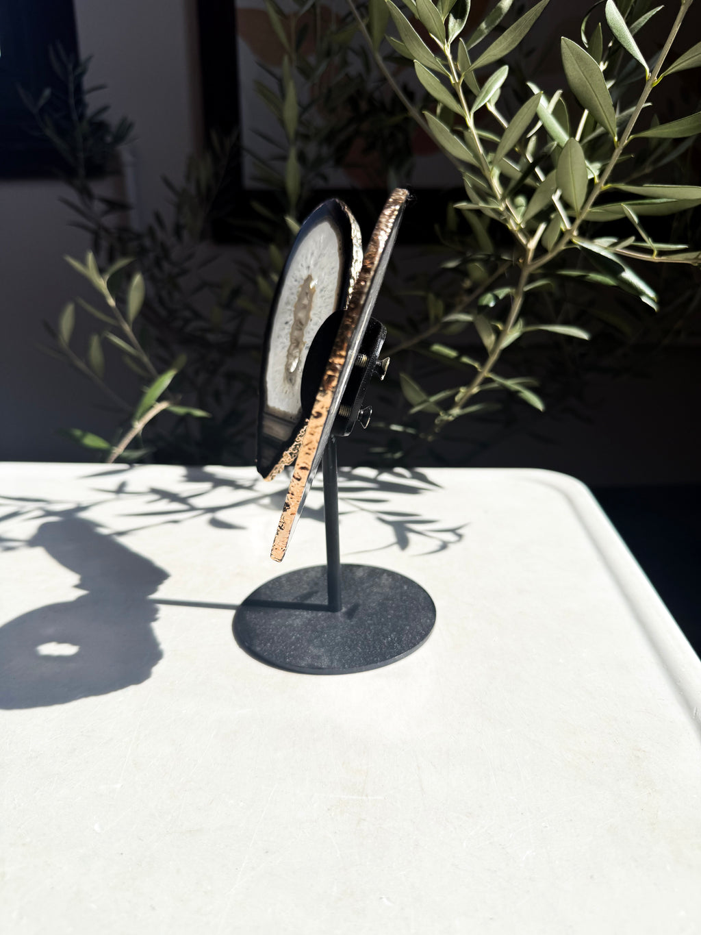 profile of gold plated agate wings on metal stand surrounded by foliage 
