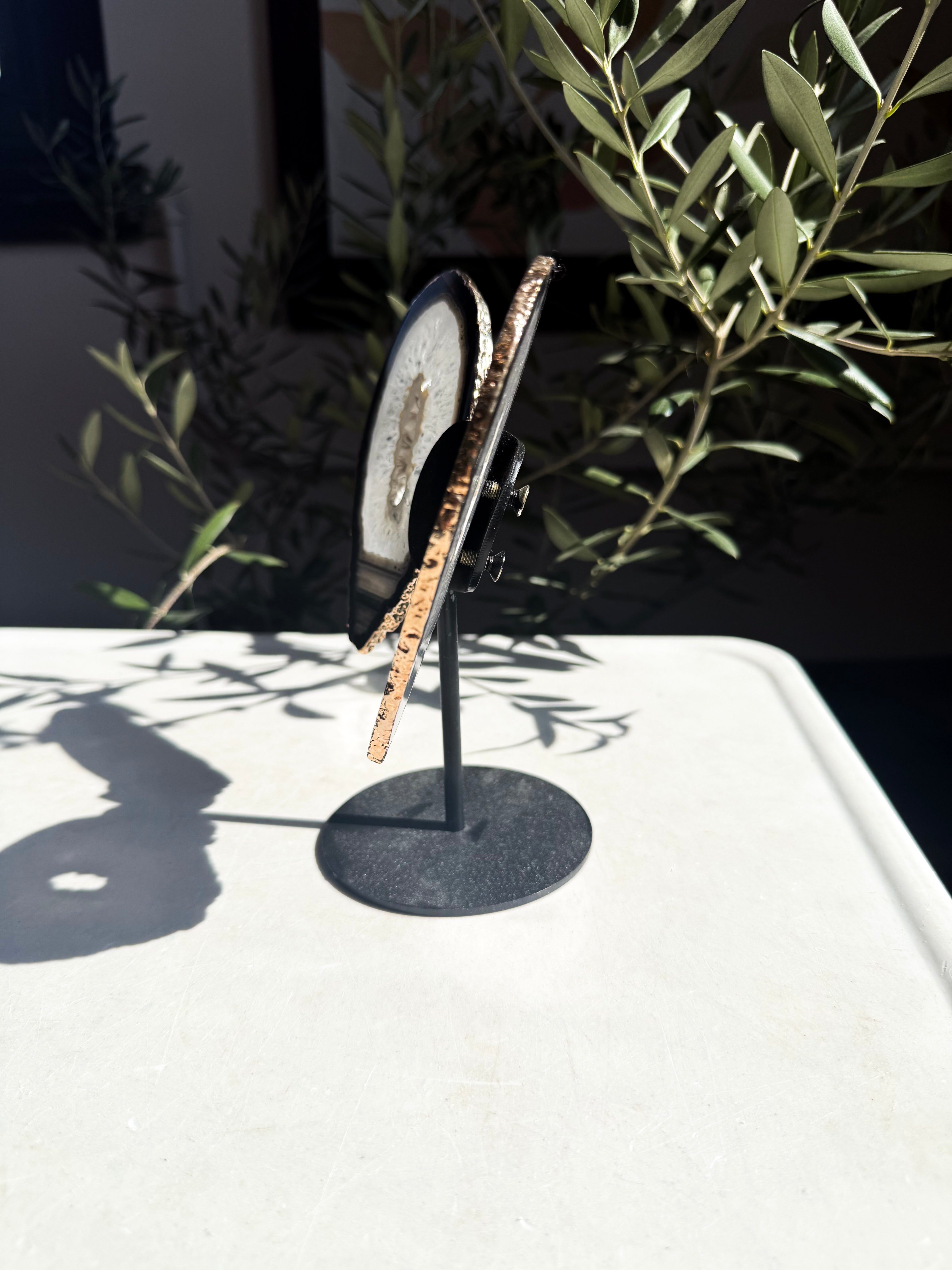 profile of gold plated agate wings on metal stand surrounded by foliage 