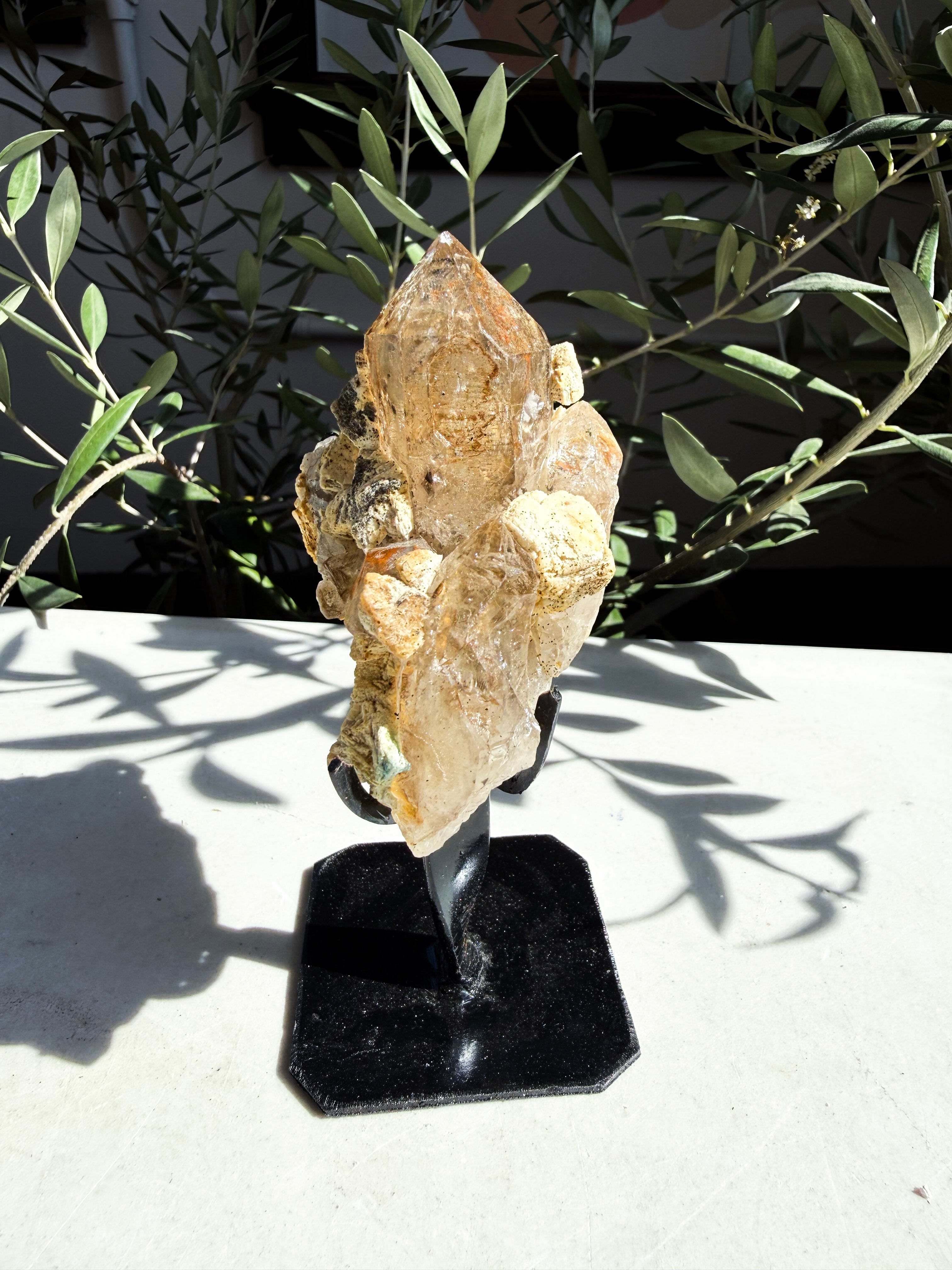 Natural smoky quartz with feldspar and lepidolite on custom stand sitting on marble counter